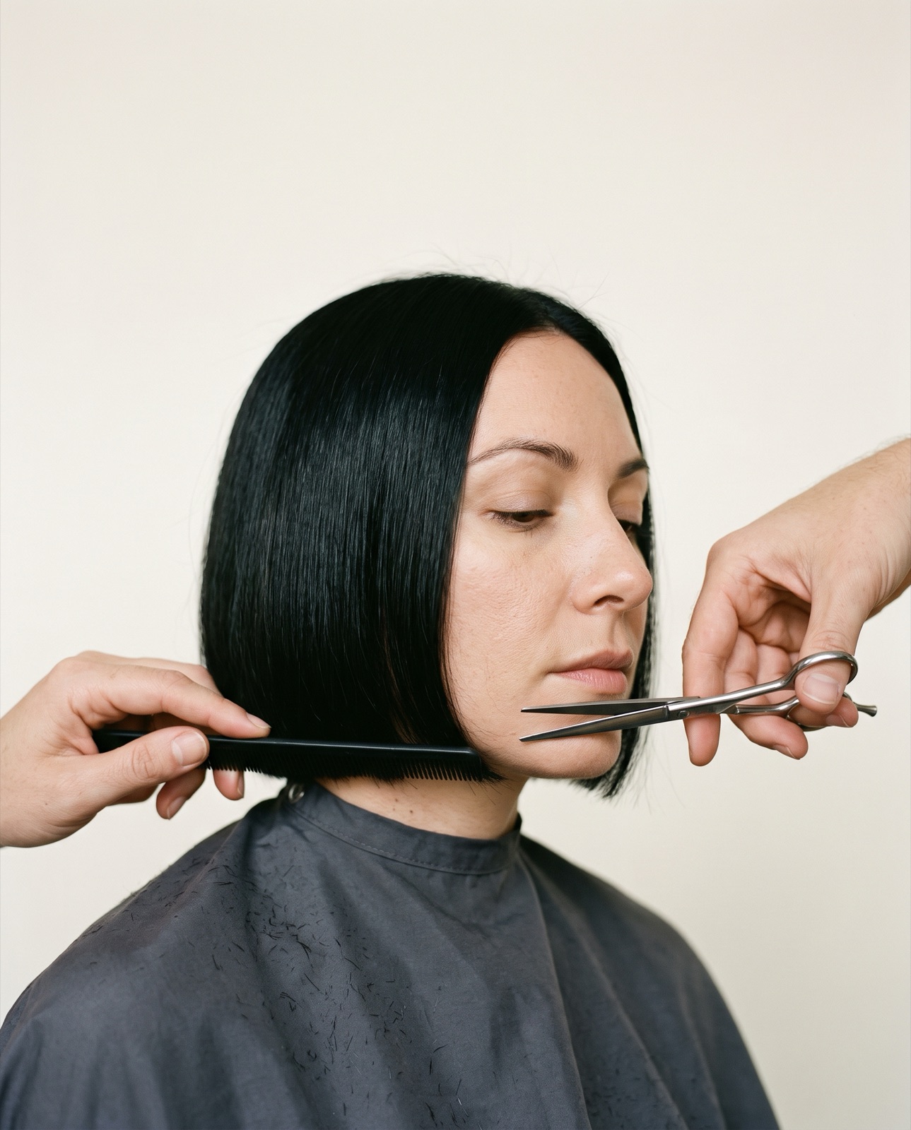 Manos de peluquero cortando con tijeras y peine una línea recta en un bob negro